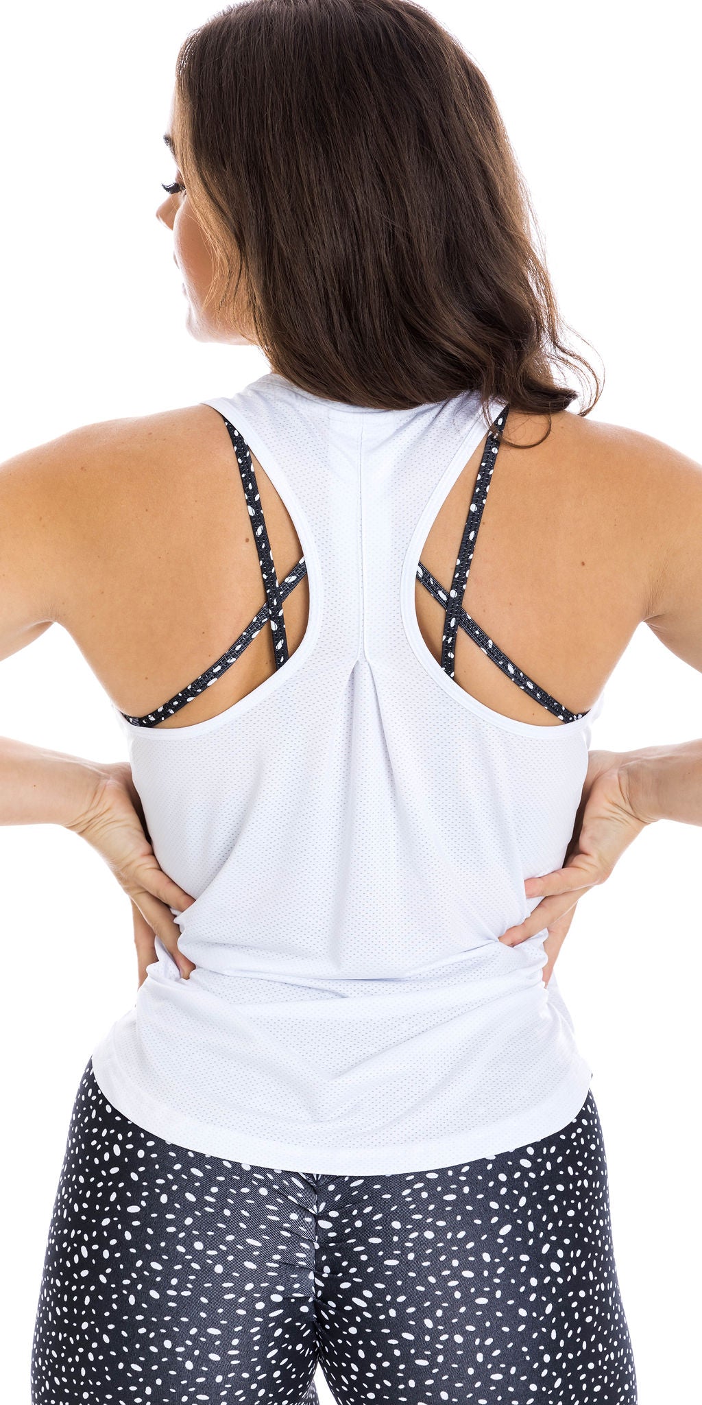 Rear view of lady in sleeveless White Meshed Racer Back Tank and black dotted leggings putting both hands on waist