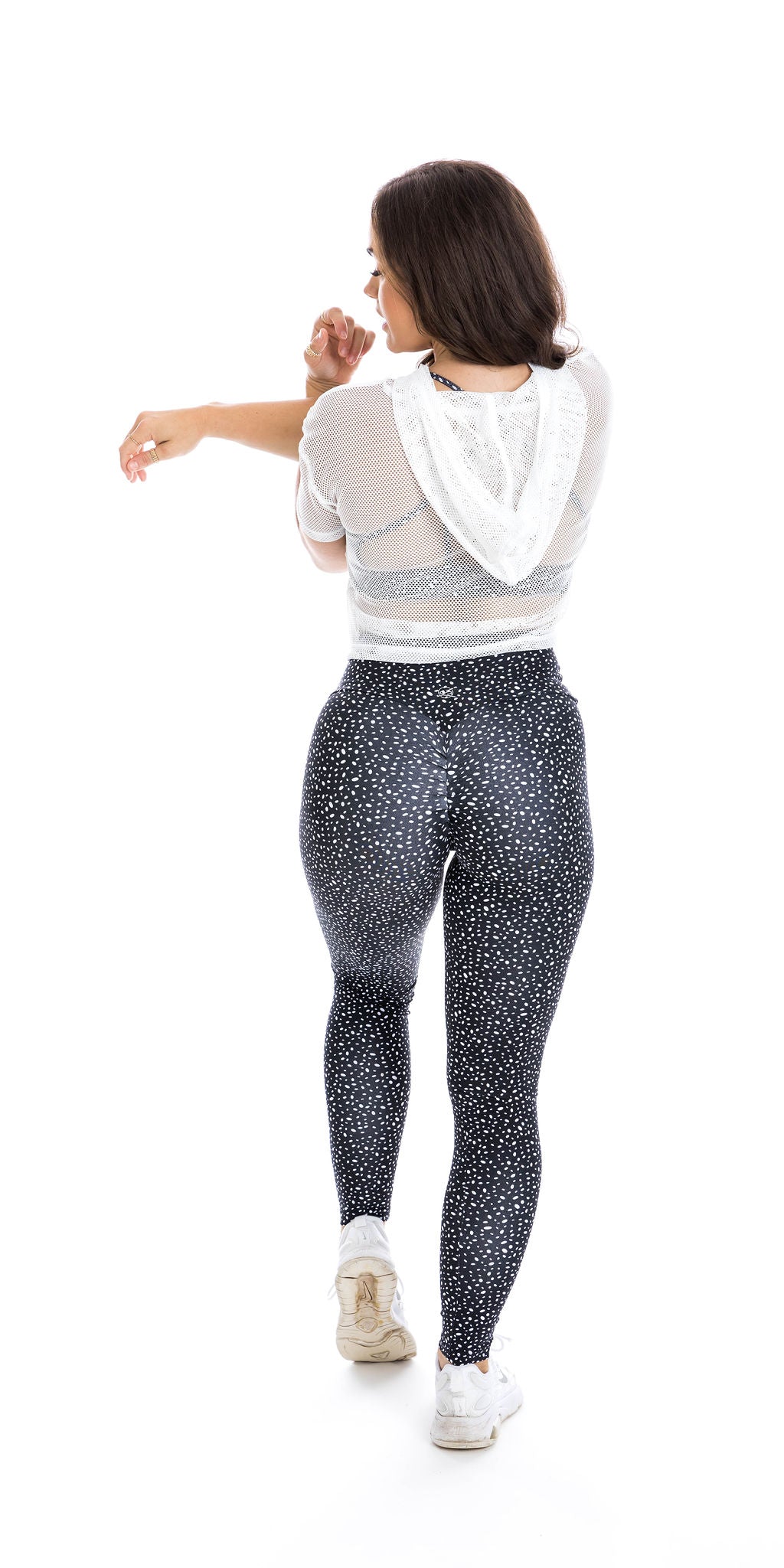 Full body rear view of lady in White Meshed Crop Hoody and black dotted leggings putting left foot forward and stretching her triceps