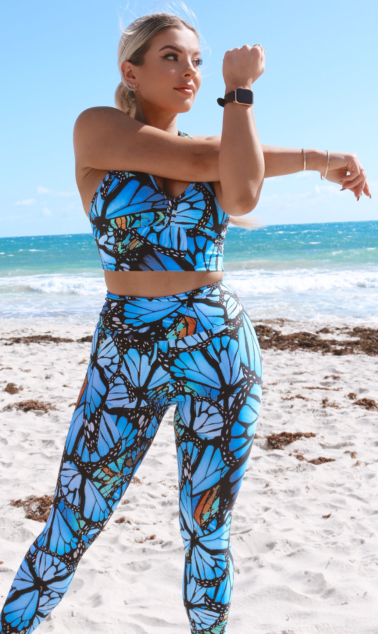 Front view of girl in blue animal print JH Butterfly Ultra High Waist 7/8 Leggings and matching bra stretching her arms