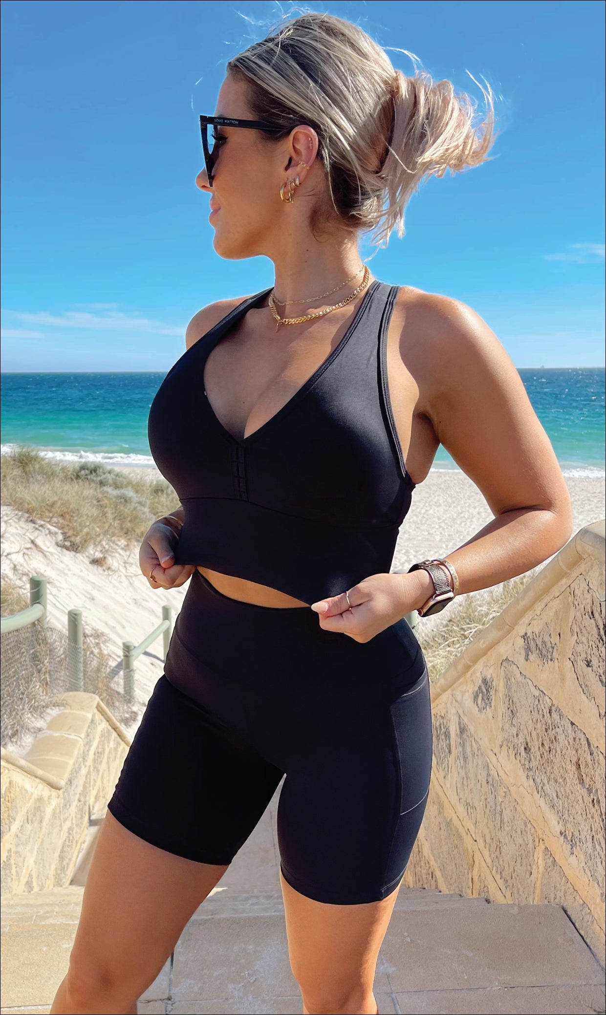 Lady on beach wearing midnight body luxe racer back bra & matching ultra high waist midi shorts with pockets