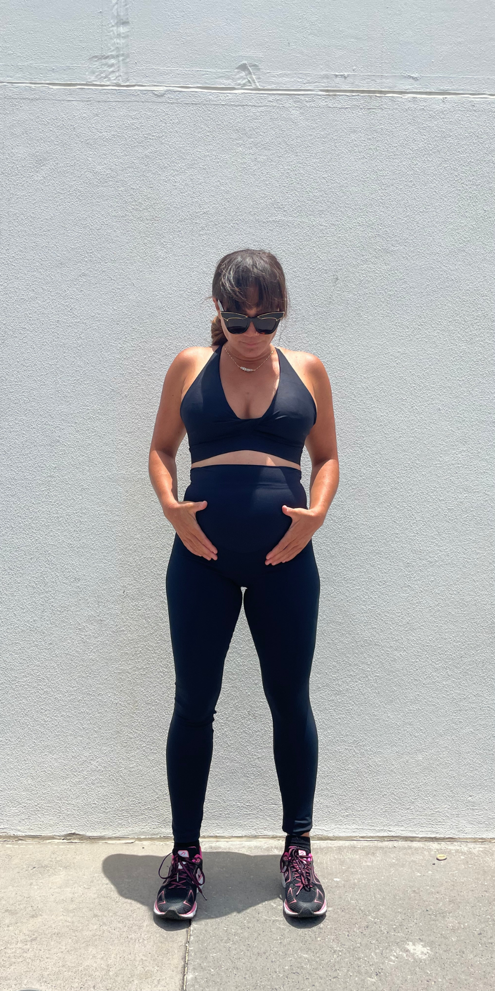 Full body front view of pregnant woman in black Midnight Maternity Leggings and matching bra holding her baby bump